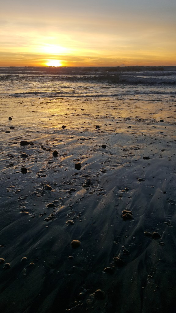 The sun is setting on a beach. 